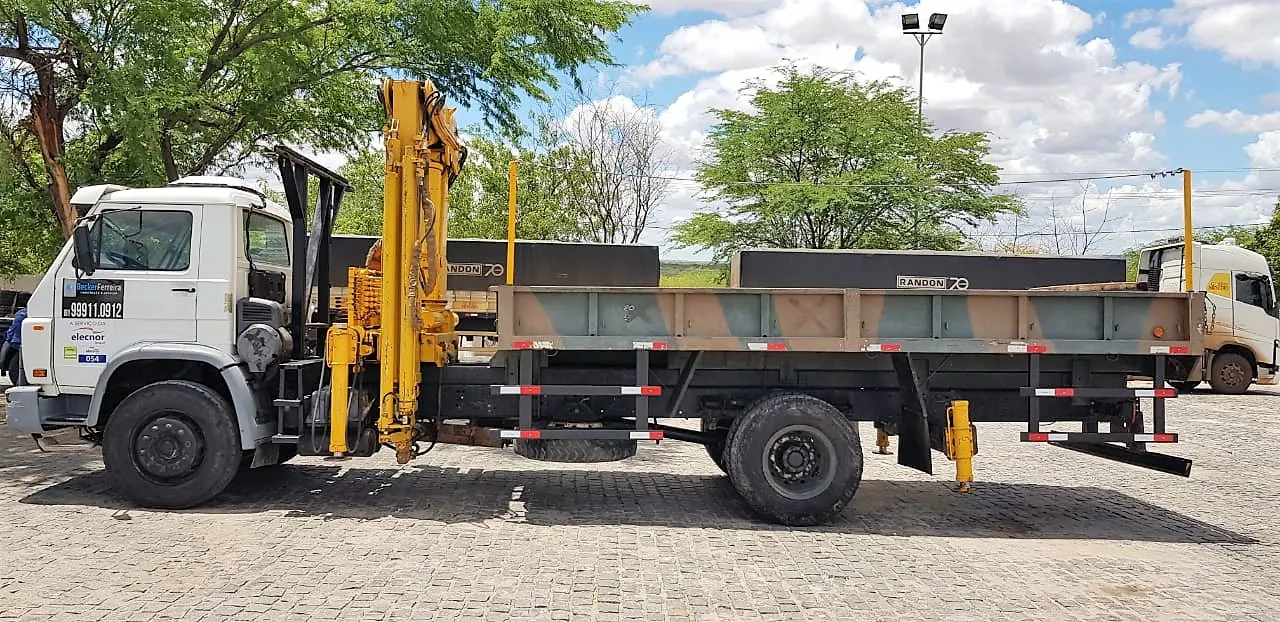 Caminhão munck da Becker Ferreira com lança amarela recolhida, sob céu aberto