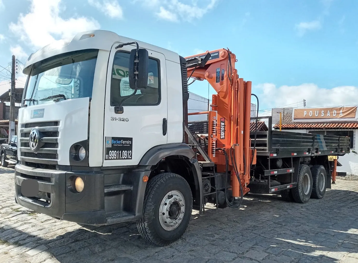 Caminhão munck traçado 6x4 da Becker Ferreira, lança laranja recolhida e carroceria de madeira vazia