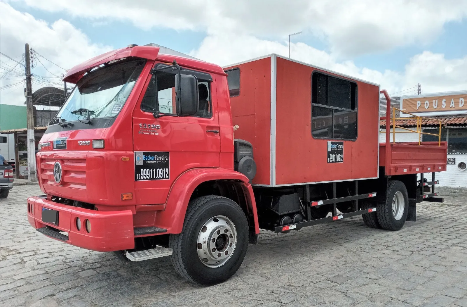 Caminhão vermelho da Becker Ferreira com baú de serviço fechado atrás da cabine e carroceria aberta na traseira